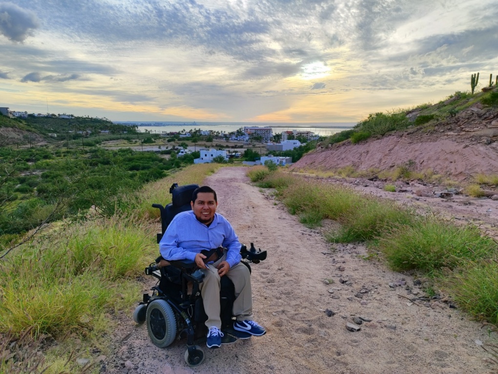 Una persona en silla de ruedas en un camino inclinado con un cerro y el cielo de fondo